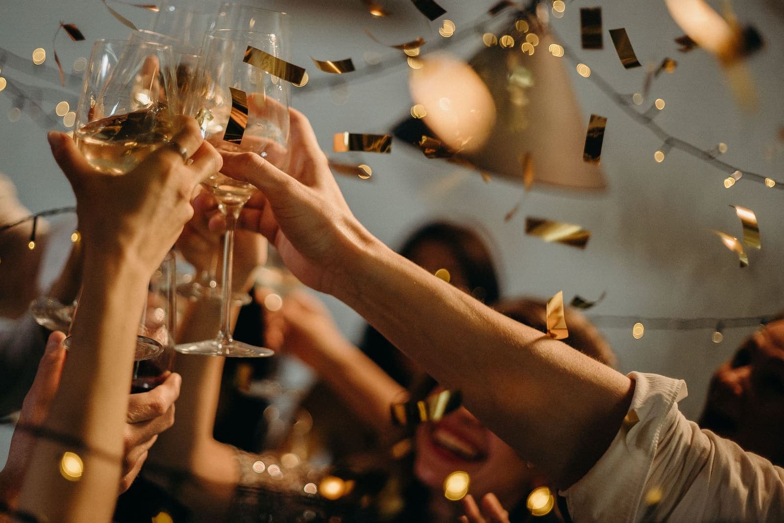 Hands raising champagne glasses in a toast as gold confetti falls