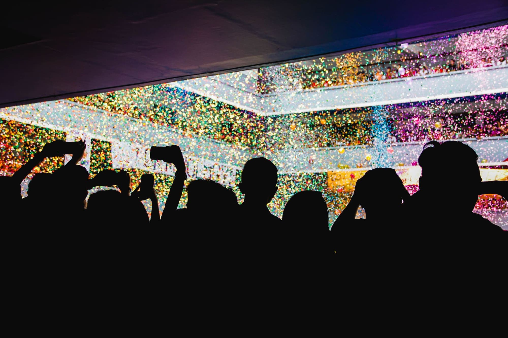 Silhouetted crowd raising their hands under a shower of colorful confetti