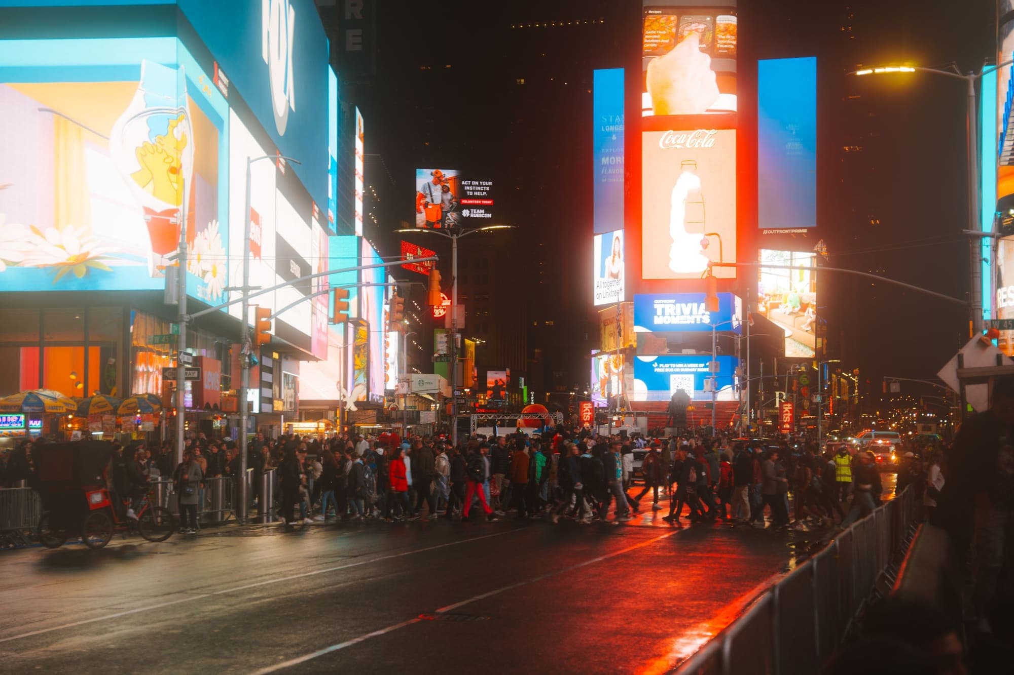 Crowds crossing Times Square beneath illuminated digital billboards at night